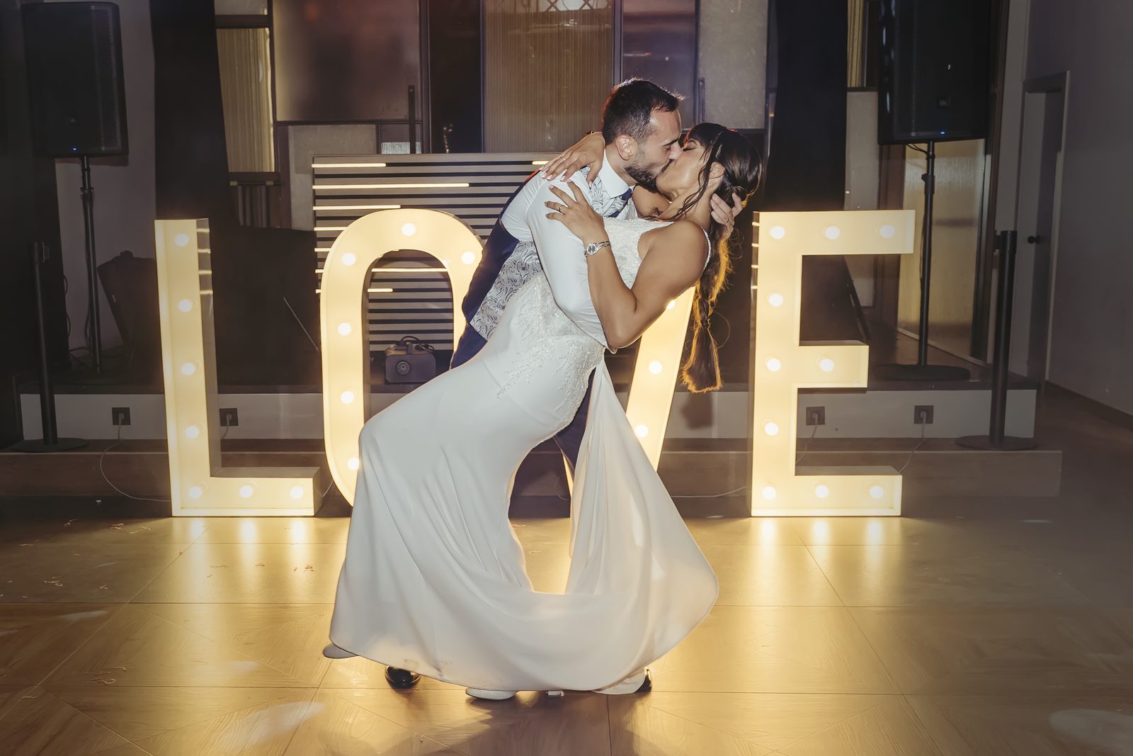 Novios besándose delante de un cartel luminoso con la palabra LOVE